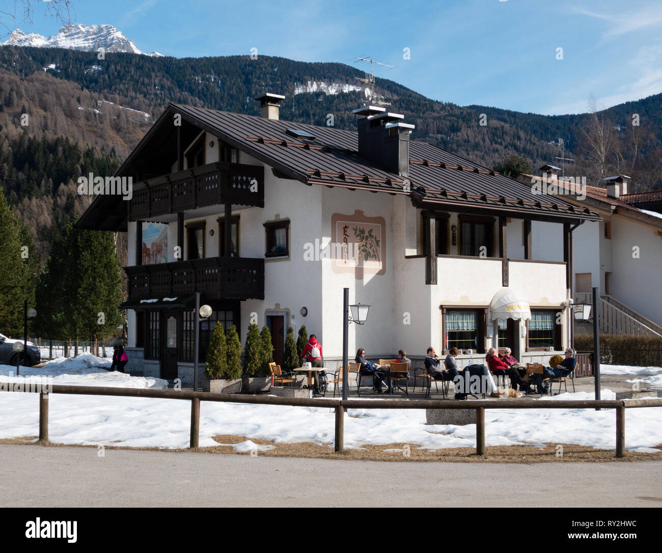 Italy cafe - people sitting outside a cafe in the snow with winter sunshine in March; Pinzolo village, Brenta Dolomites, northern Italy Europe Stock Photo