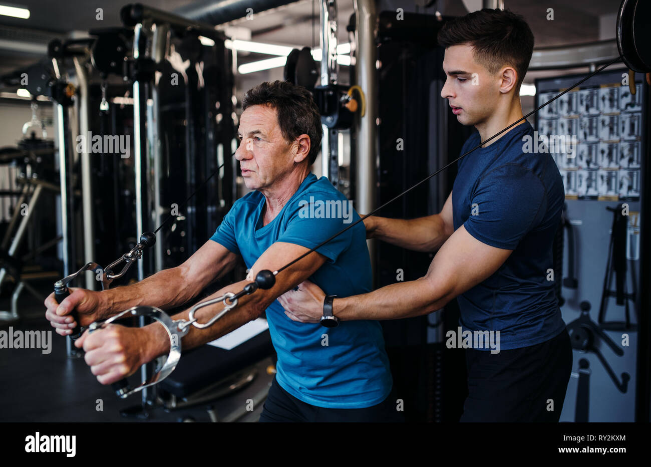 Man Using Strength A senior man with a young trainer doing strength workout exercise in ...