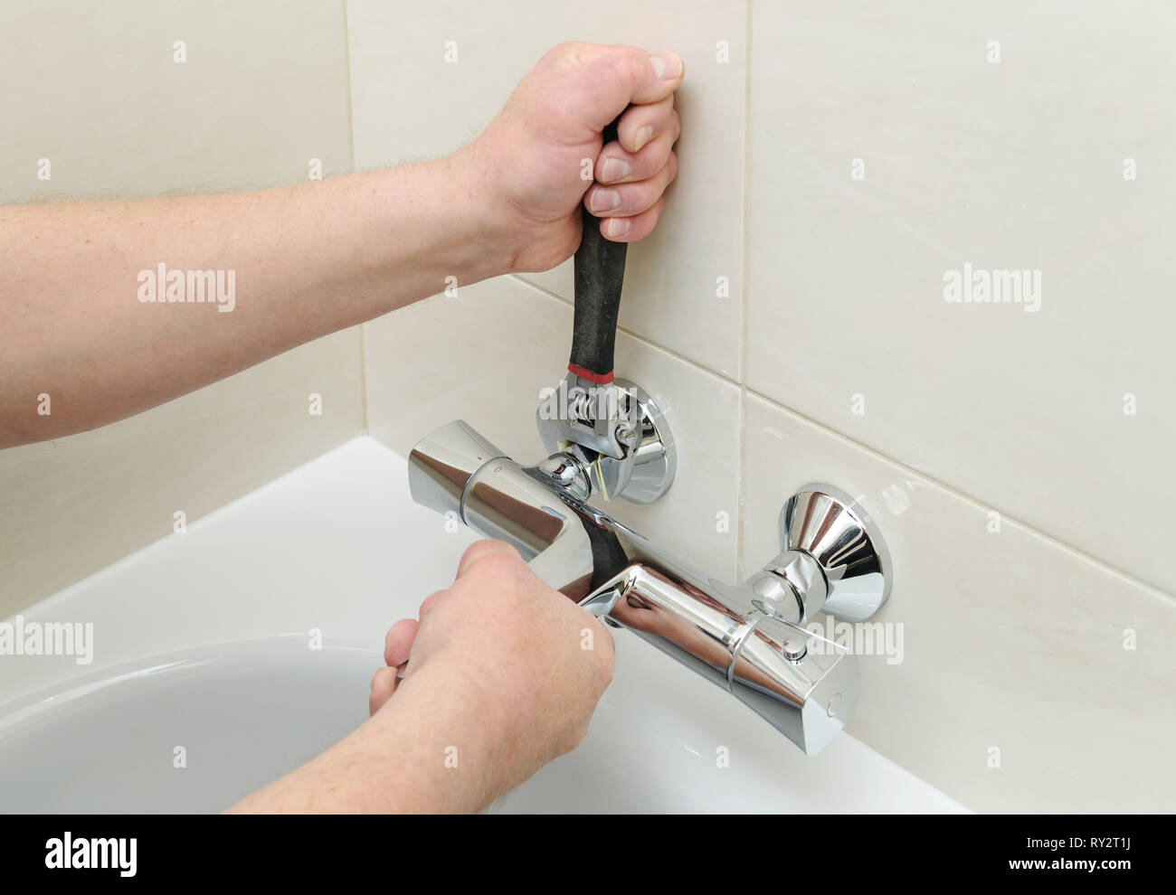 Installing faucet with thermostat. Man's hands are fixing bath tap into place. Stock Photo