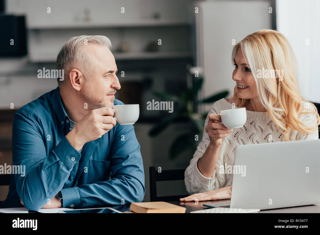 cheerful couple holding cups with drinks and looking at each other at home Stock Photo