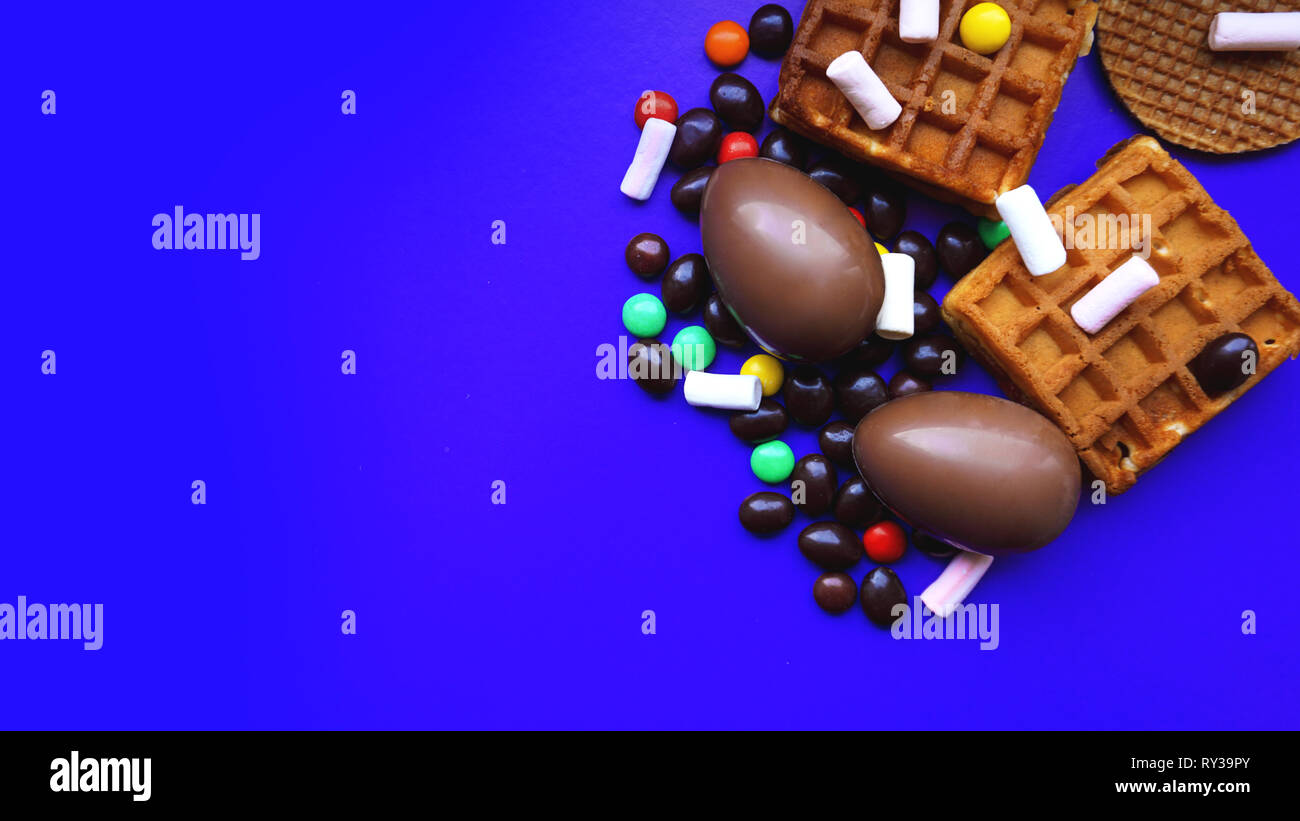 Delicious chocolate easter eggs, waffles, sweets on dark blue background Stock Photo