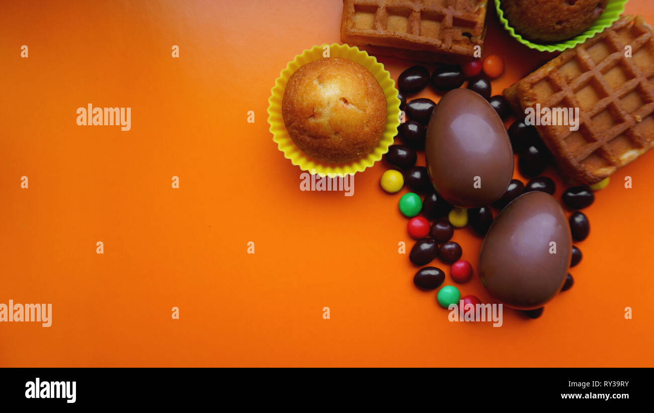 Delicious chocolate easter eggs, waffles, sweets on orange background Stock Photo