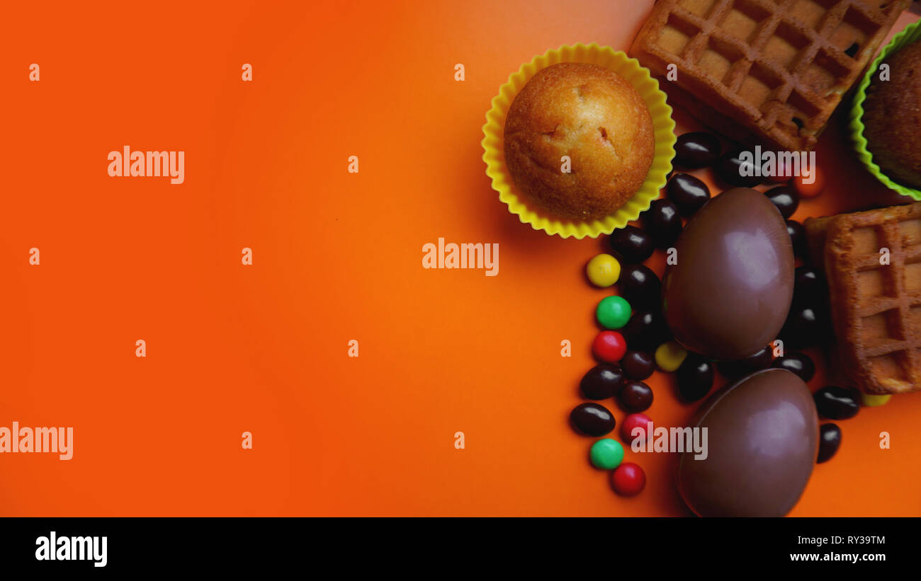 Delicious chocolate easter eggs, waffles, sweets on orange background Stock Photo