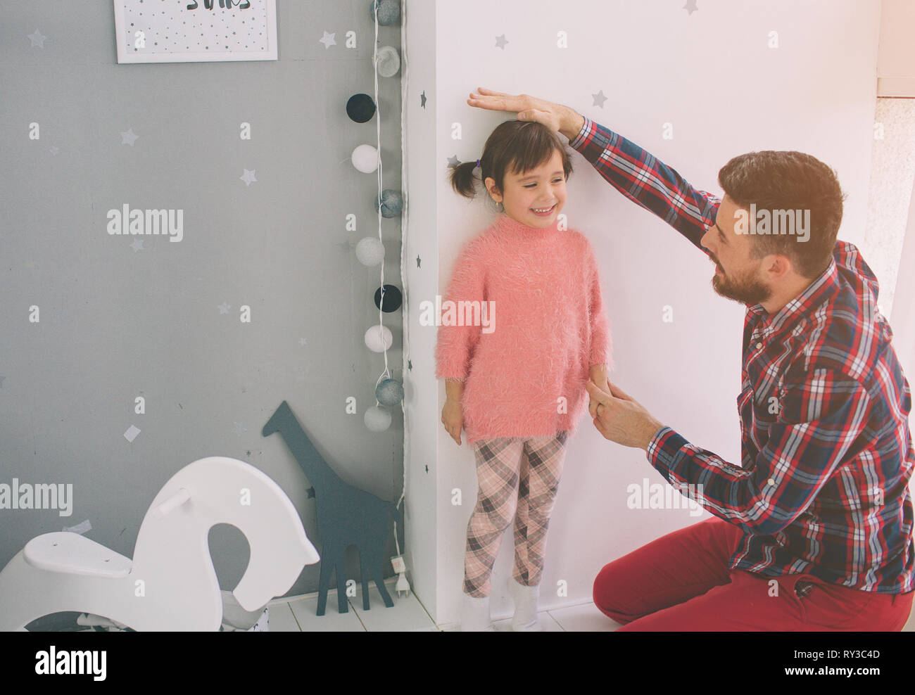Father is measuring his baby height on the wall. Cute little daughter and her handsome young dad are playing together in child's room Stock Photo