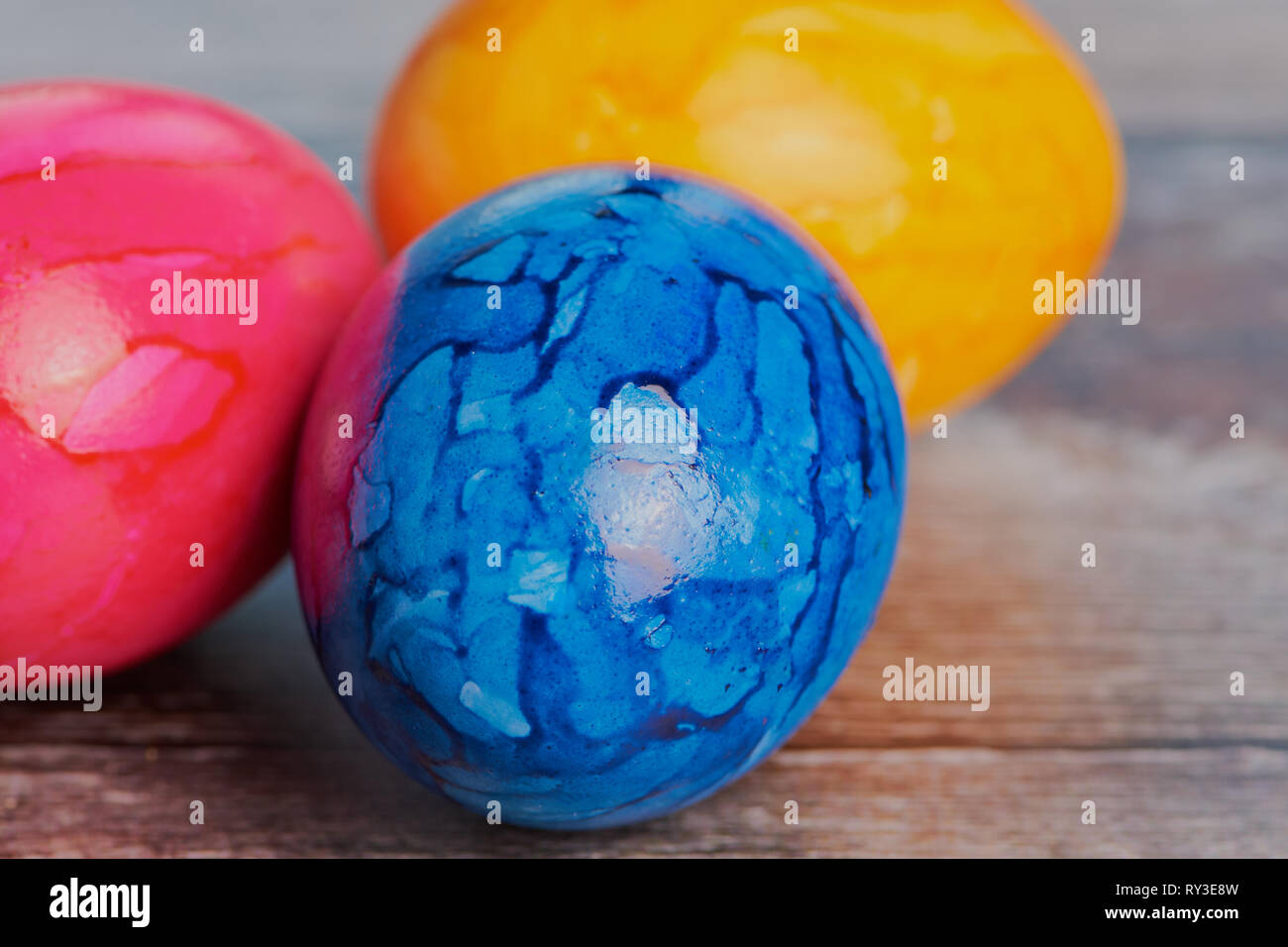three colored easter eggs on a brown wooden surface Stock Photo