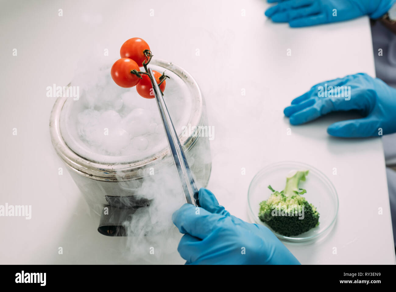 cropped view of female scientists experimenting with dry ice and vegetables in chemical