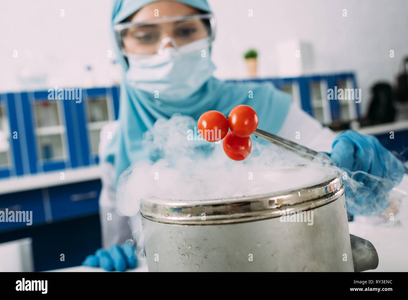 female muslim scientist holding tomatoes with tweezers over pot with