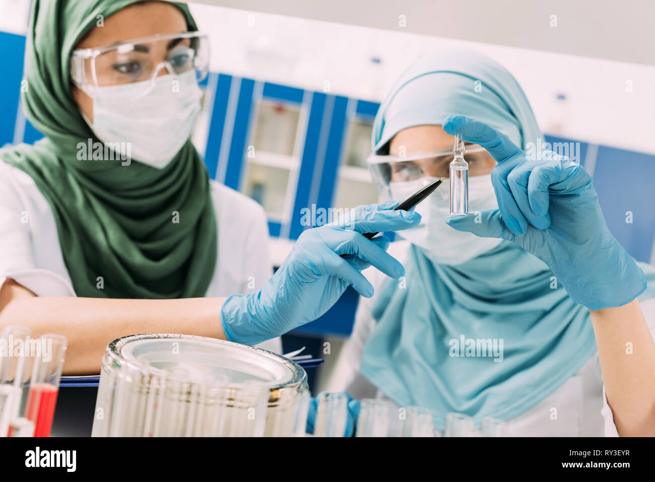 female muslim scientists in medical masks holding glass ampoule during ...