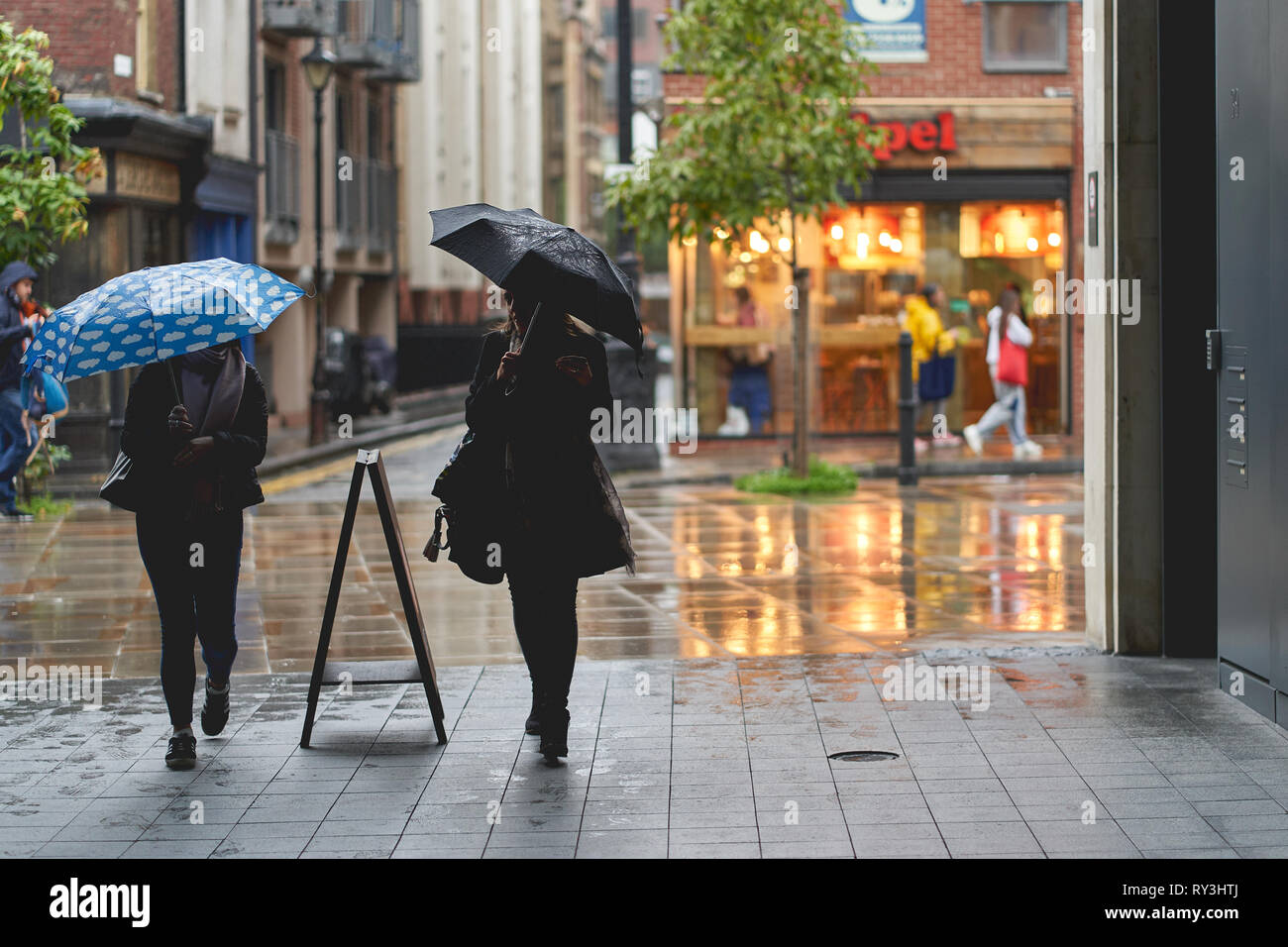 London, UK - March, 2019. Young girls walking with umbrellas under the rain in Shoreditch. Stock Photo