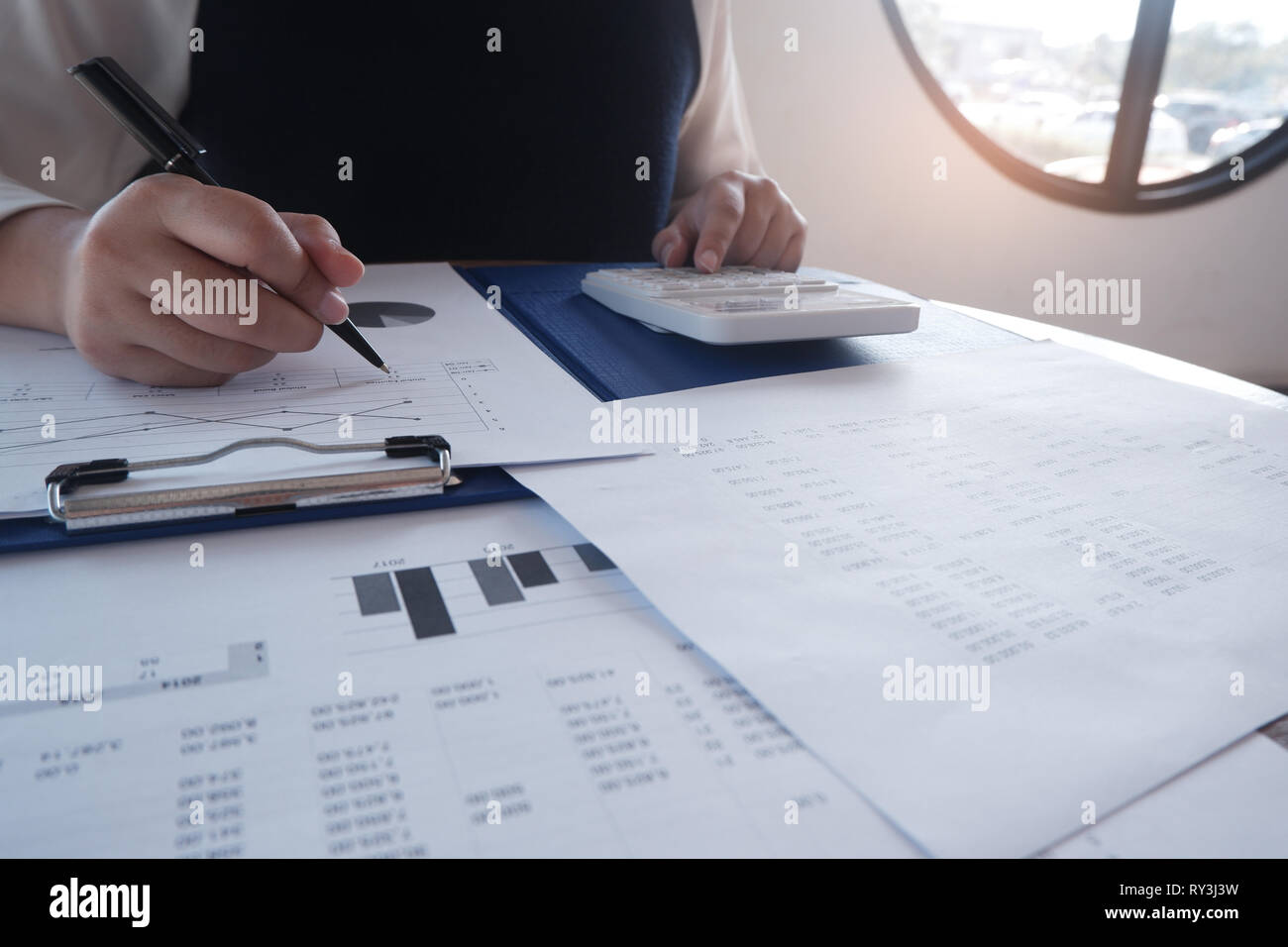 Female working in office, studying using calculator and writing something with documents and chart on table Stock Photo