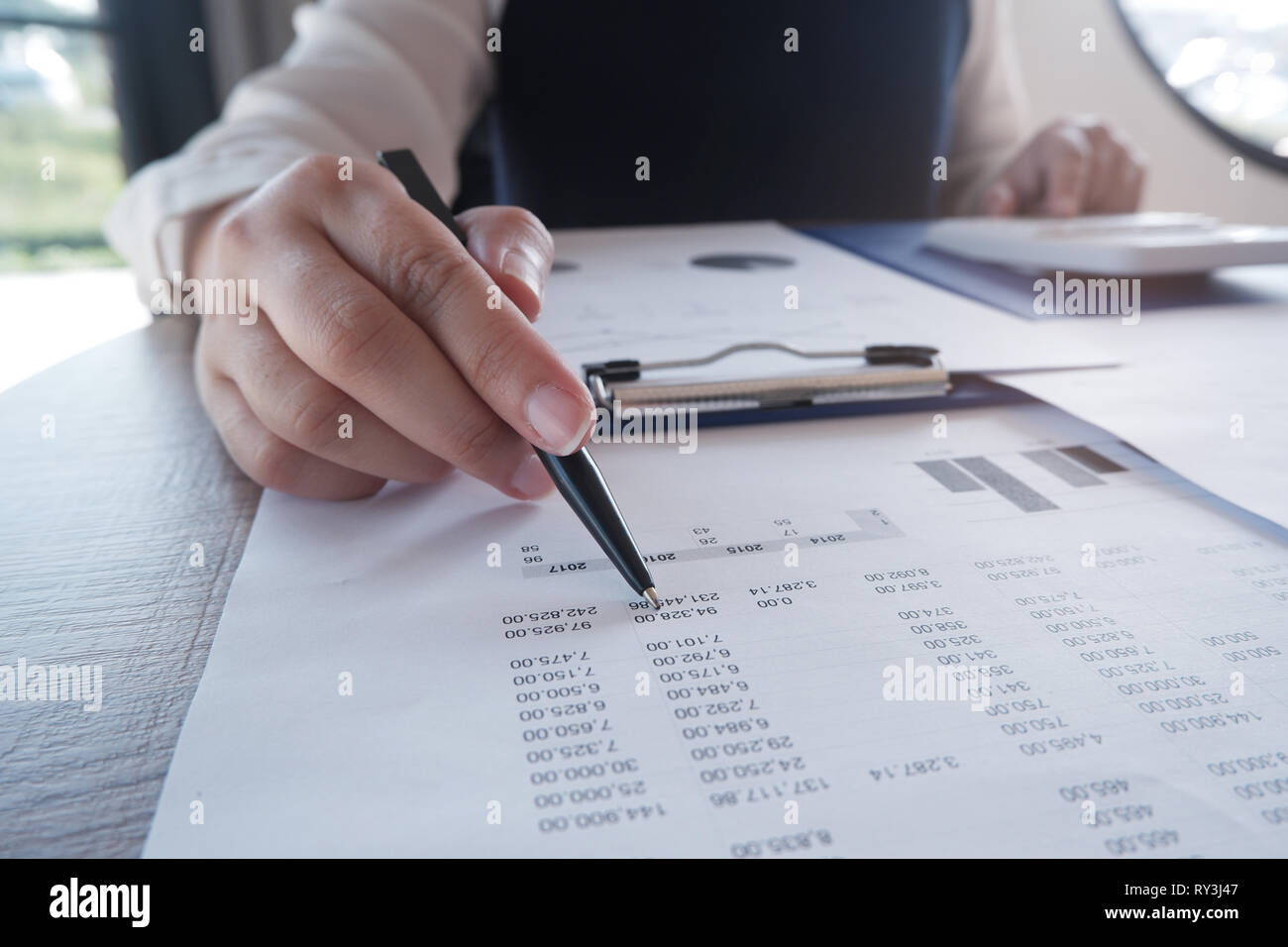 Female working in office, studying using calculator and writing something with documents and chart on table Stock Photo