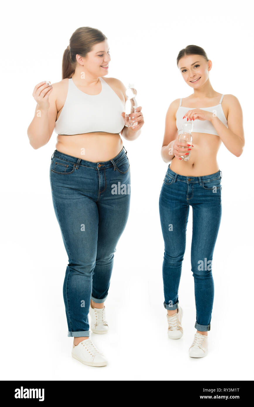 smiling slim and overweight women in jeans holding bottles with water isolated on white Stock