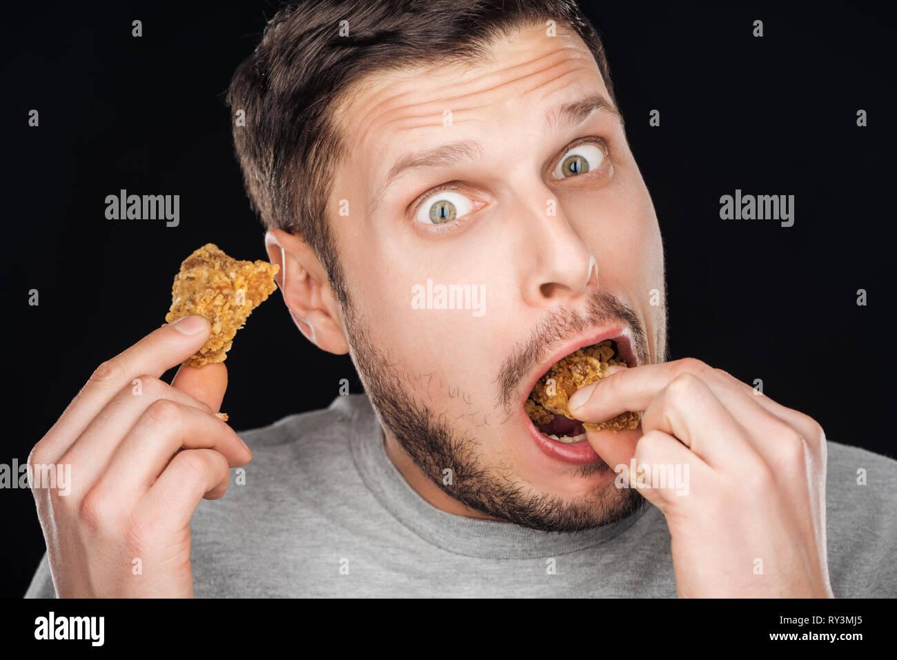 emotional man eating tasty chicken nuggets while looking at camera isolated on black Stock Photo