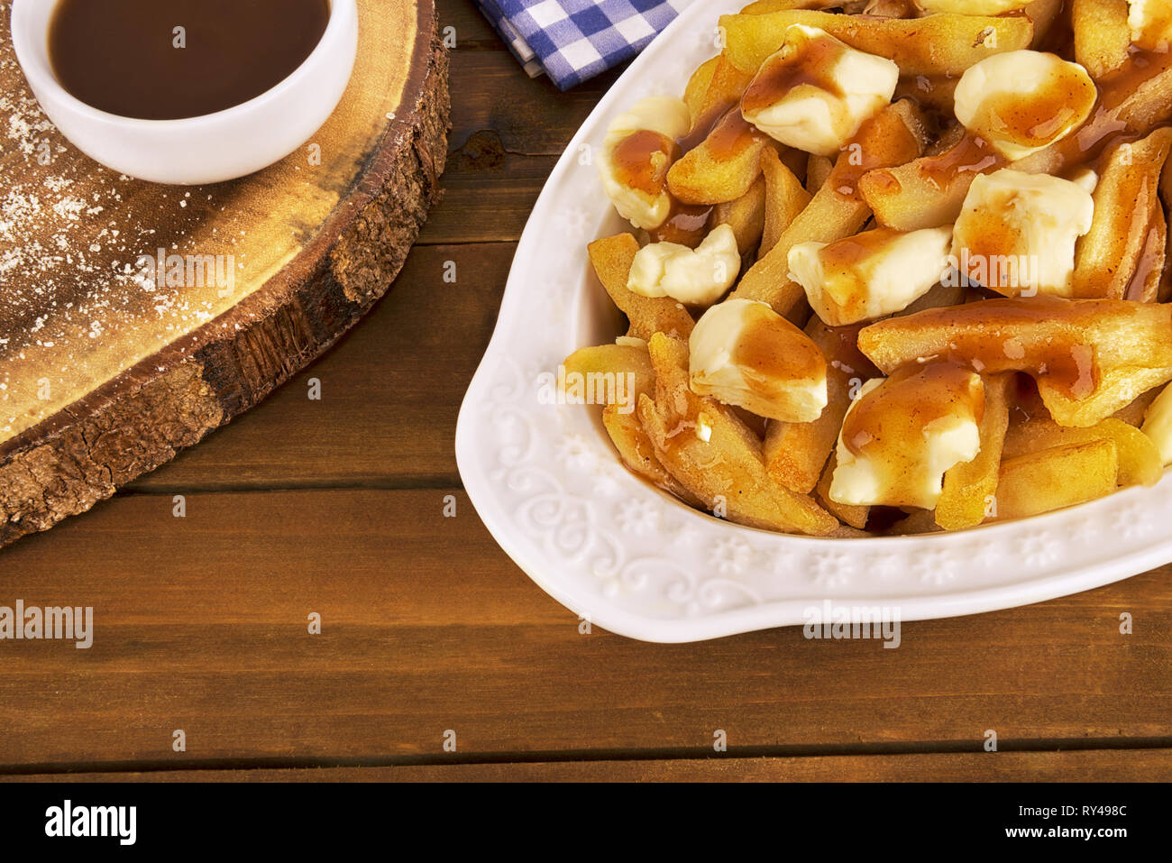 Poutine plate on a wooden background. Cooked with french fries, gravy and curd cheese. Canadian cuisine. Stock Photo