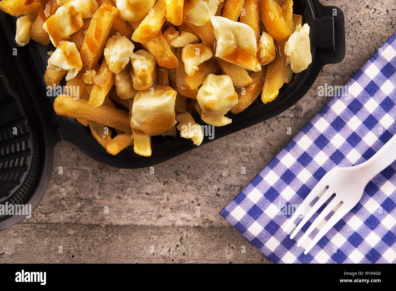 Poutine in a takeout container. Cooked with french fries, beef gravy and curd cheese. Canadian cuisine. Stock Photo