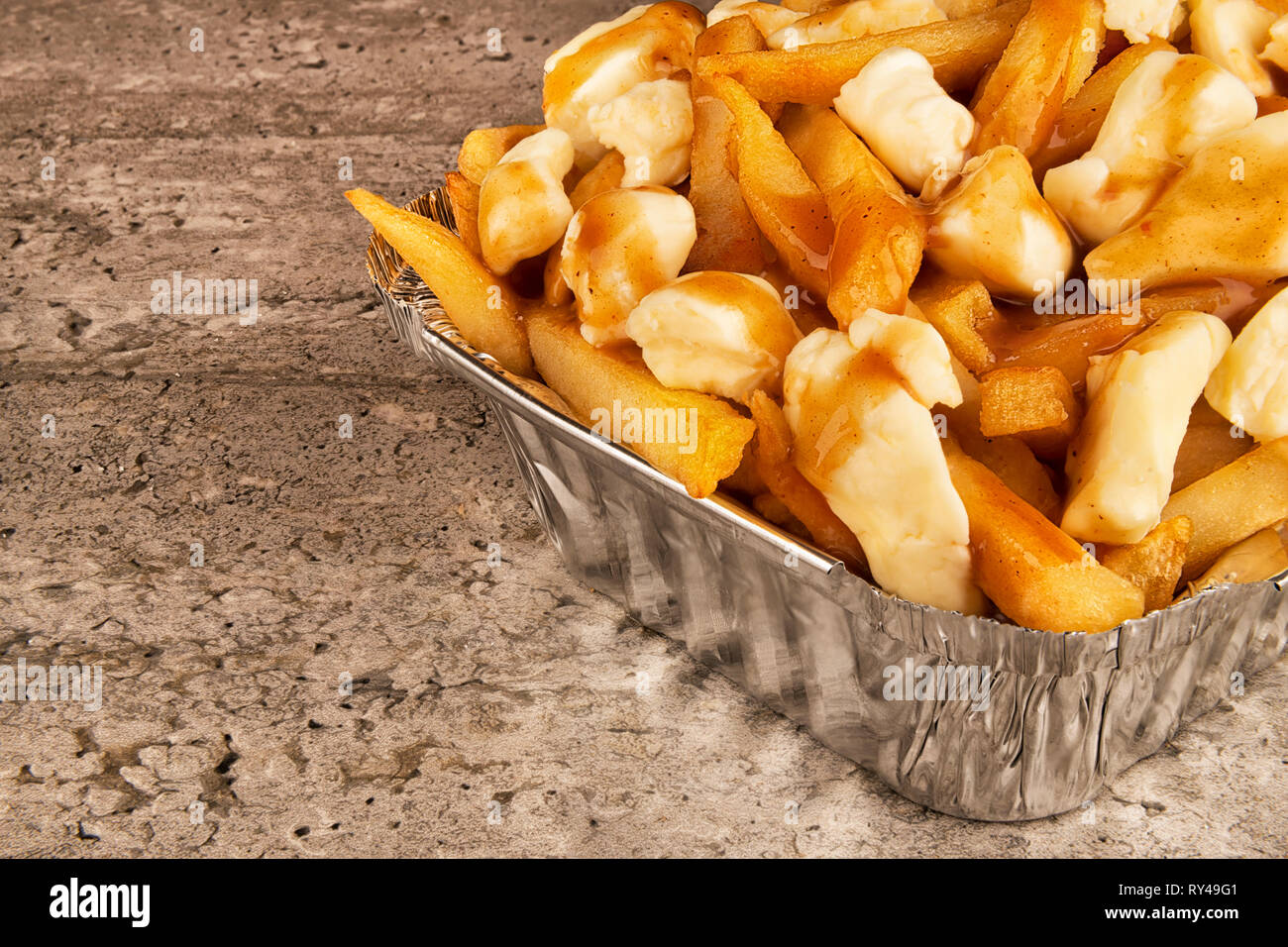 Partial close up on a poutine in a takeout container. Cooked with french fries, beef gravy and curd cheese. Stock Photo