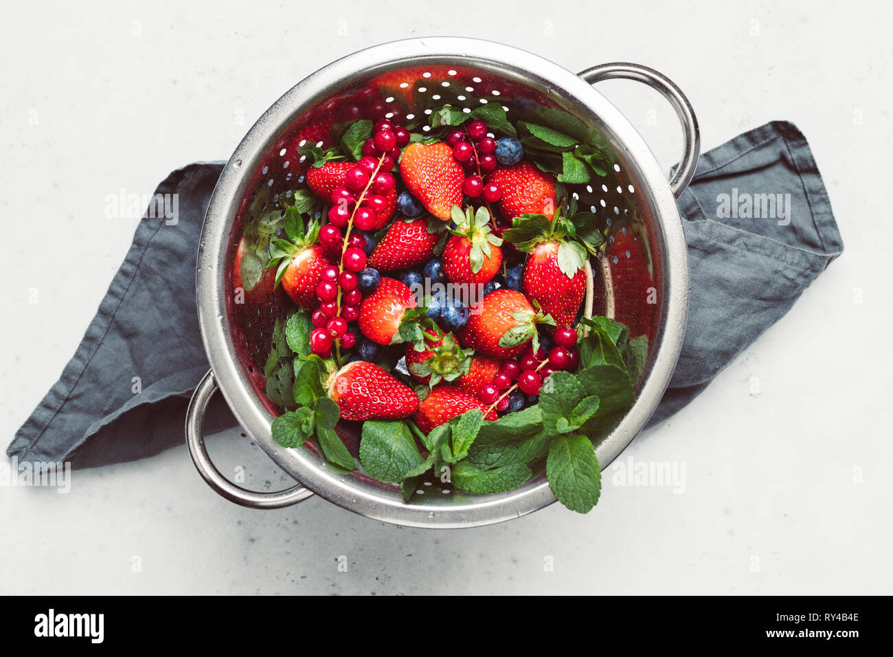Metal colander with fresh berries above white table. Strawberry ...