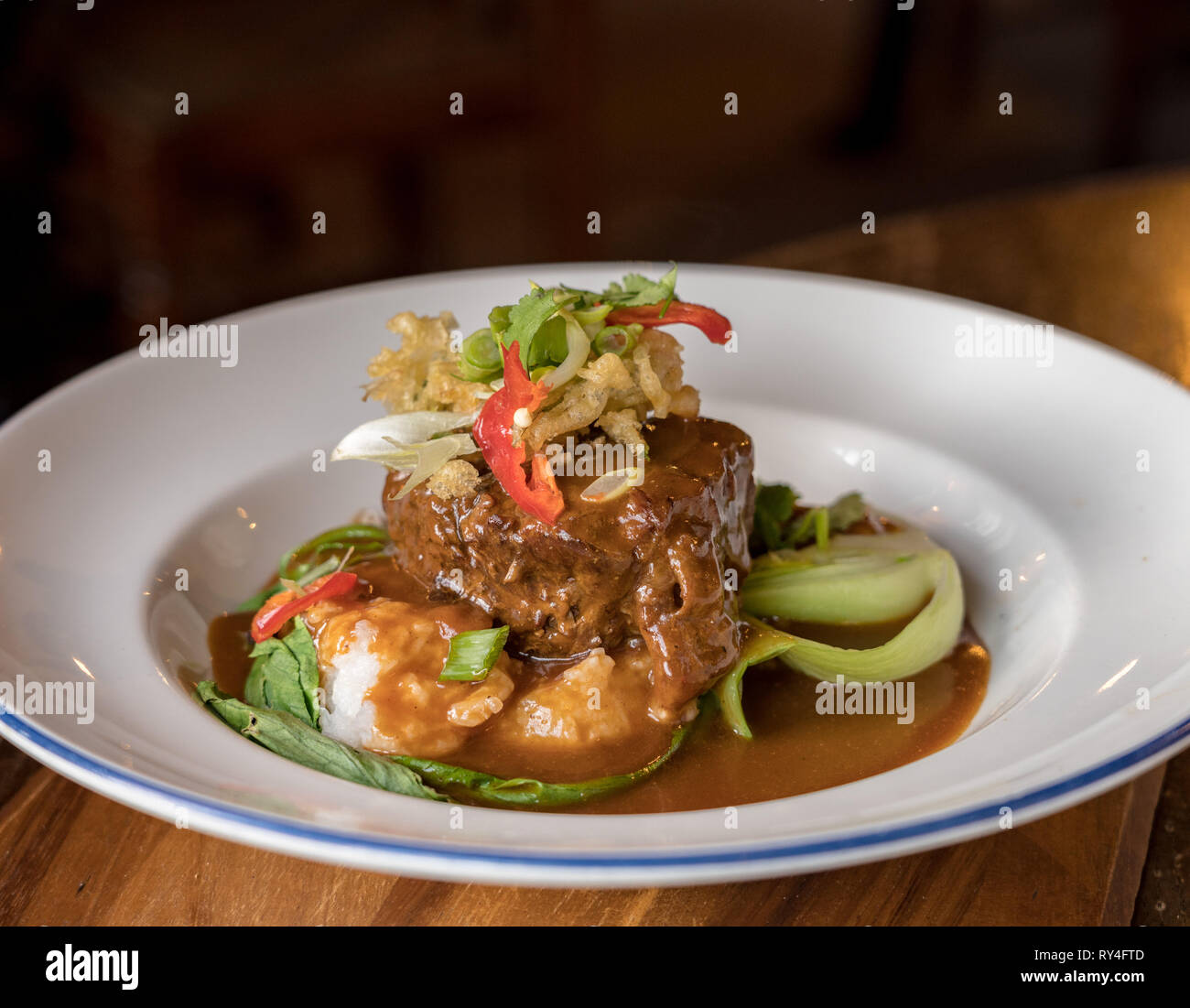 Beef Rendang curry in white bowl on pub table Stock Photo