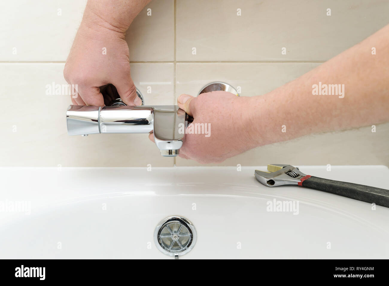 Installing faucet with thermostat. Man's hands are fixing bath tap into place. Stock Photo