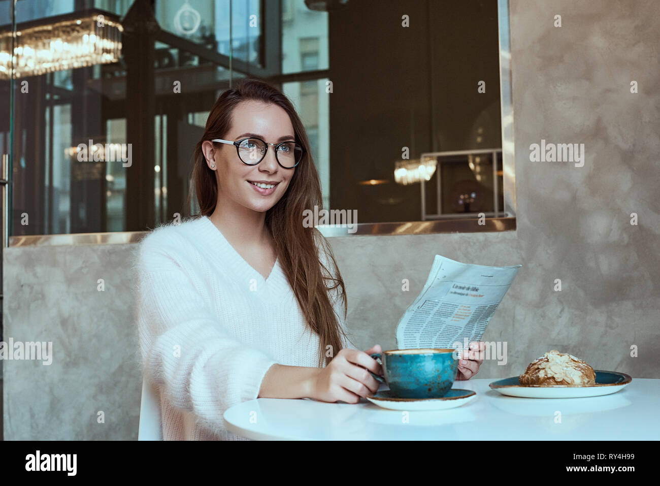 Young woman having a breakfast with coffee and croissant reading newspaper outdoors at the typical french cafe terrace in France Stock Photo