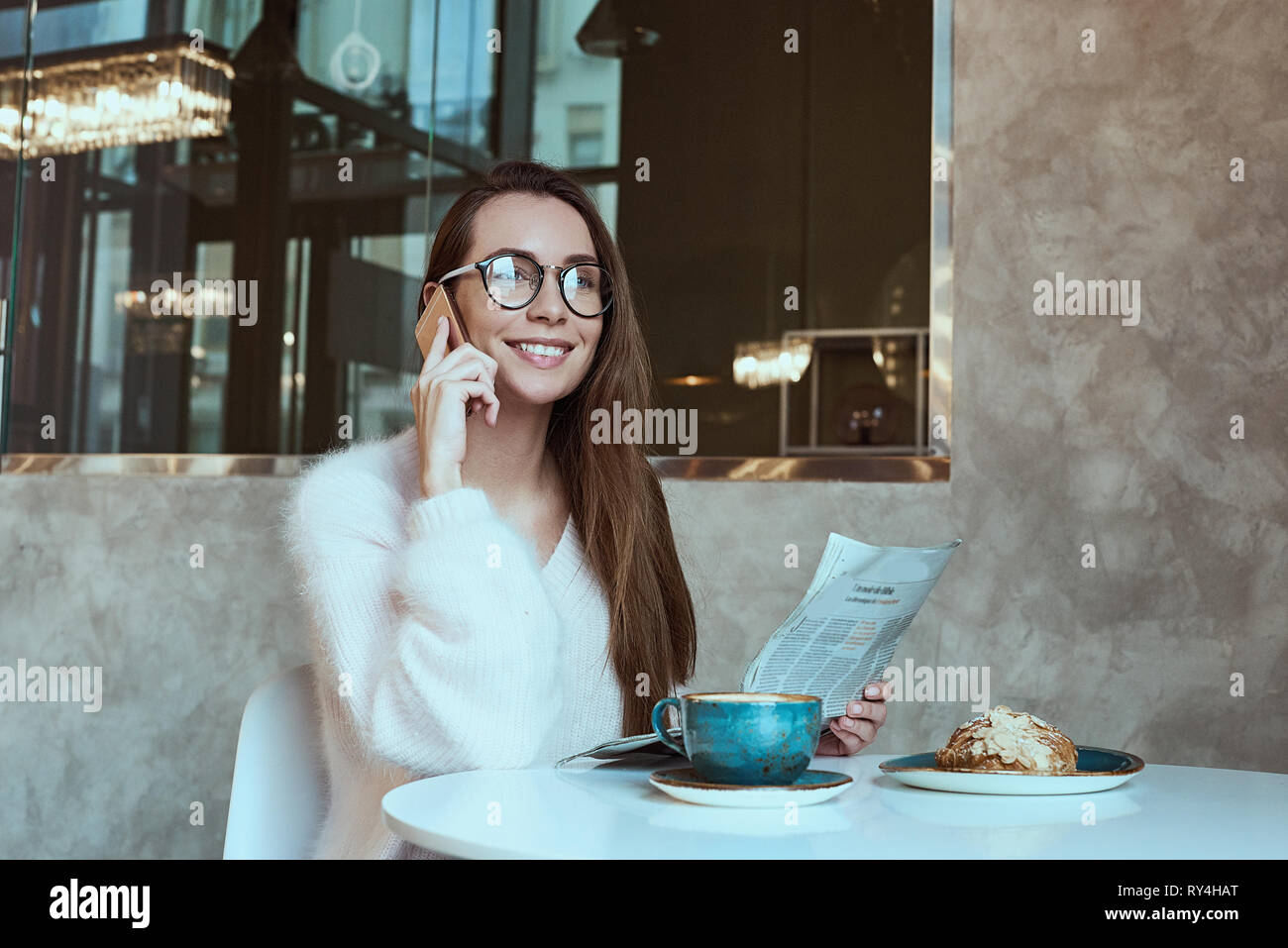 Young woman having a breakfast with coffee and croissant reading newspaper outdoors at the typical french cafe terrace in France Stock Photo