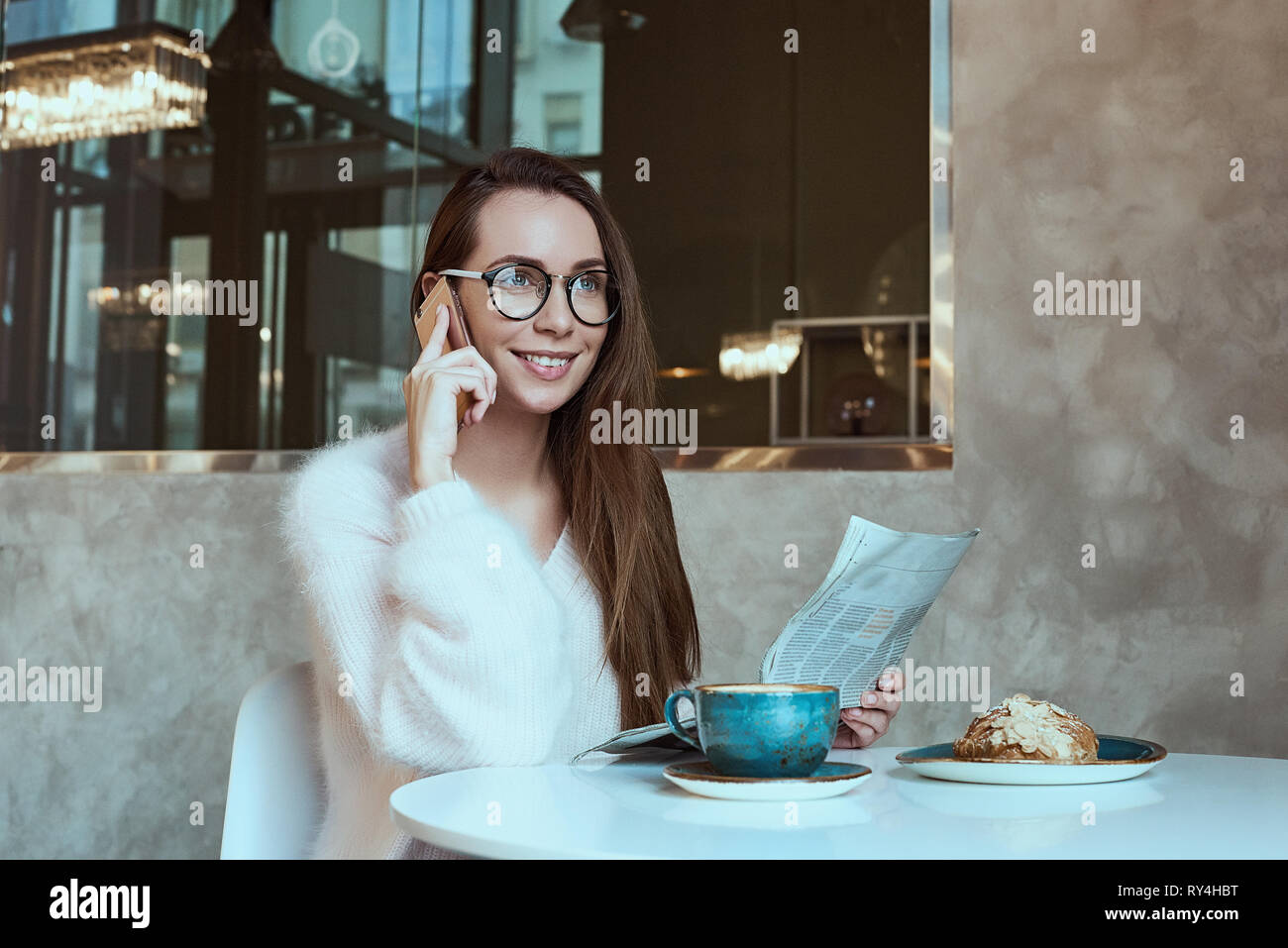 Young woman having a breakfast with coffee and croissant reading newspaper outdoors at the typical french cafe terrace in France Stock Photo