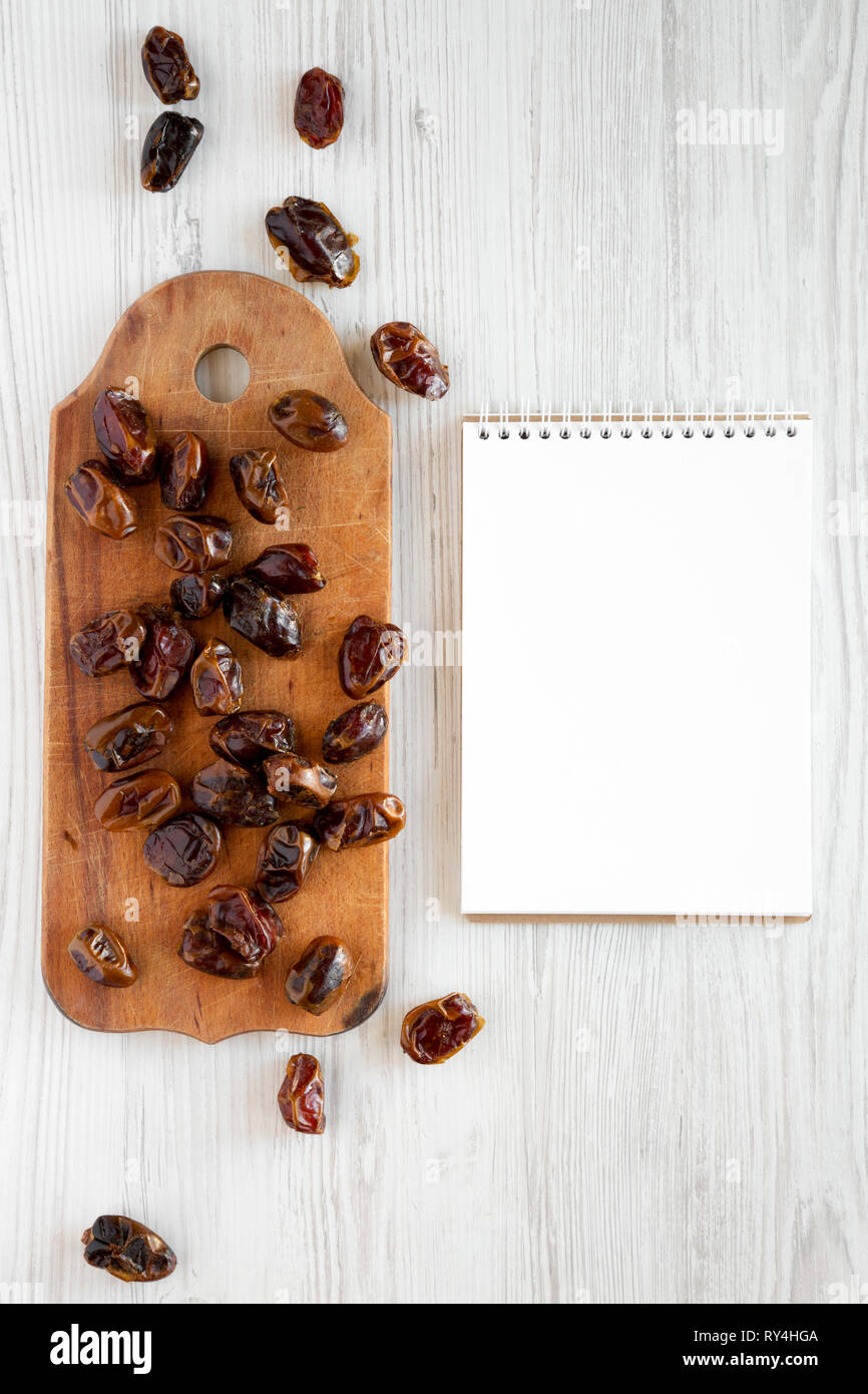 Dried dates on rustic wooden board, blank notepad over white wooden ...