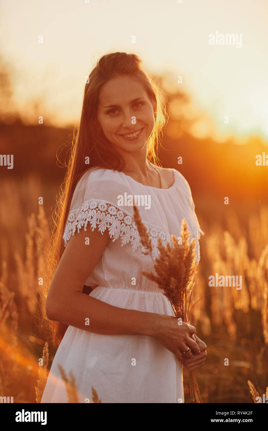 Portrait of a beautiful girl in a white dress in the field at sunset ...