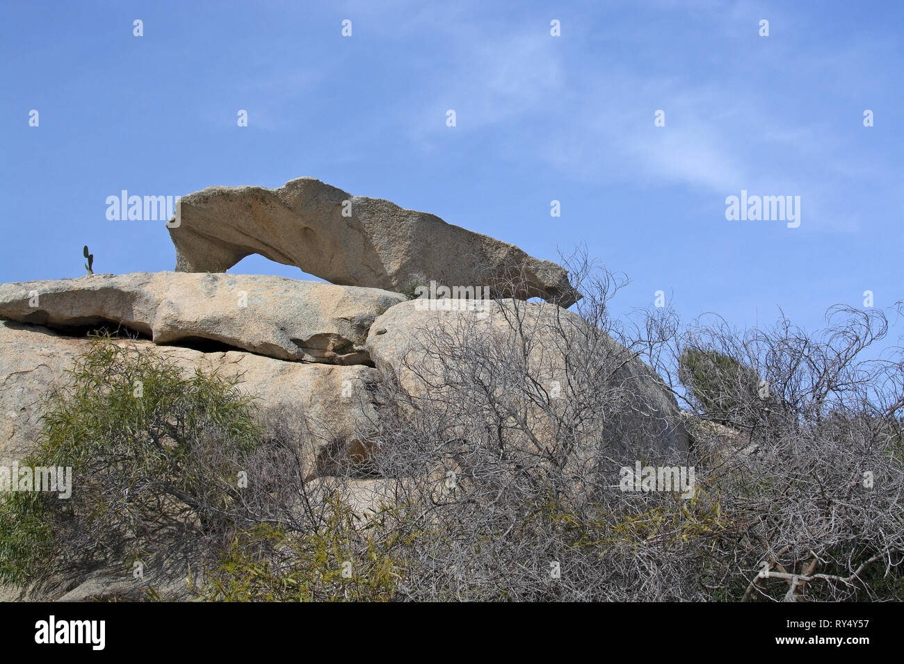 Slab of granite rock lying on top of eroded cliff with blue sky wispy cloud in Costa Smeralda, Sardinia, Italy. Stock Photo