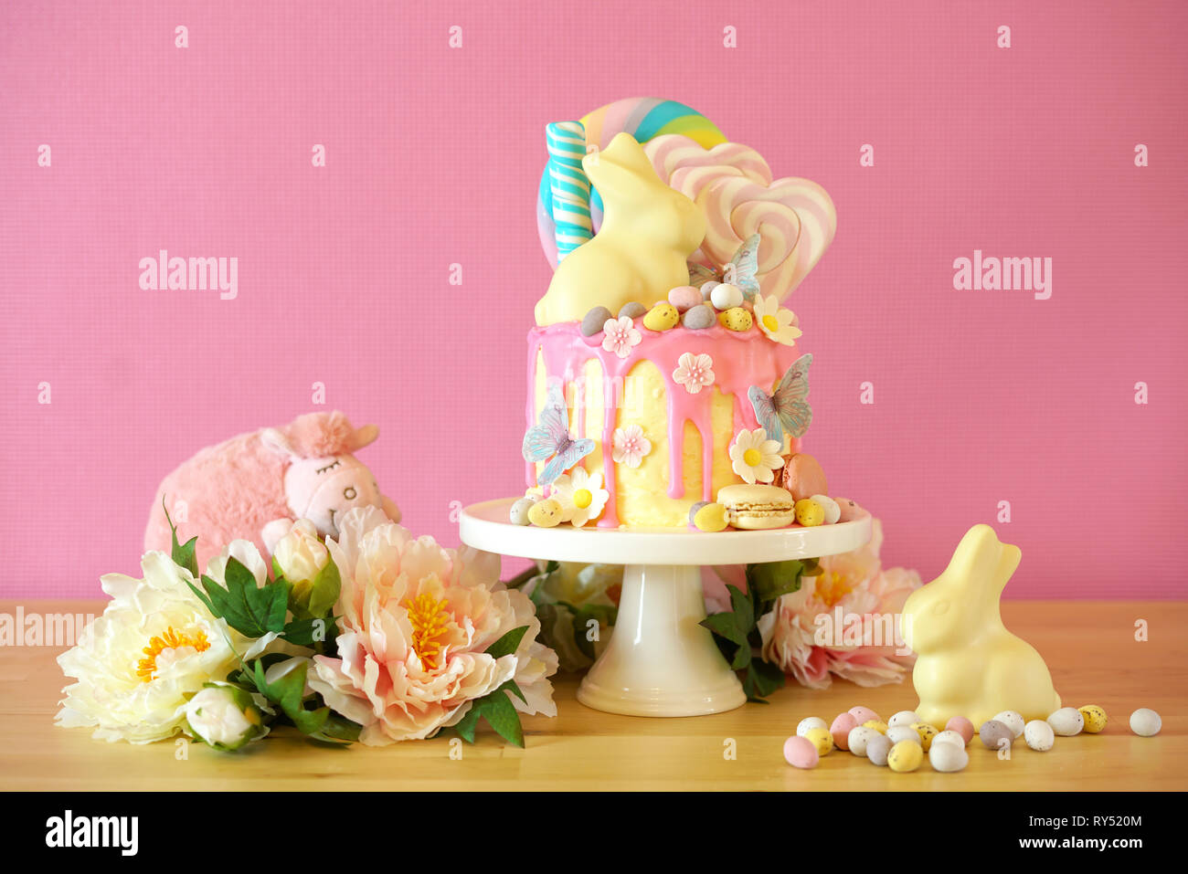 On-trend Easter theme candy land drip cake decorated with lollipops, candy eggs and white chocolate bunny in party table setting. Stock Photo