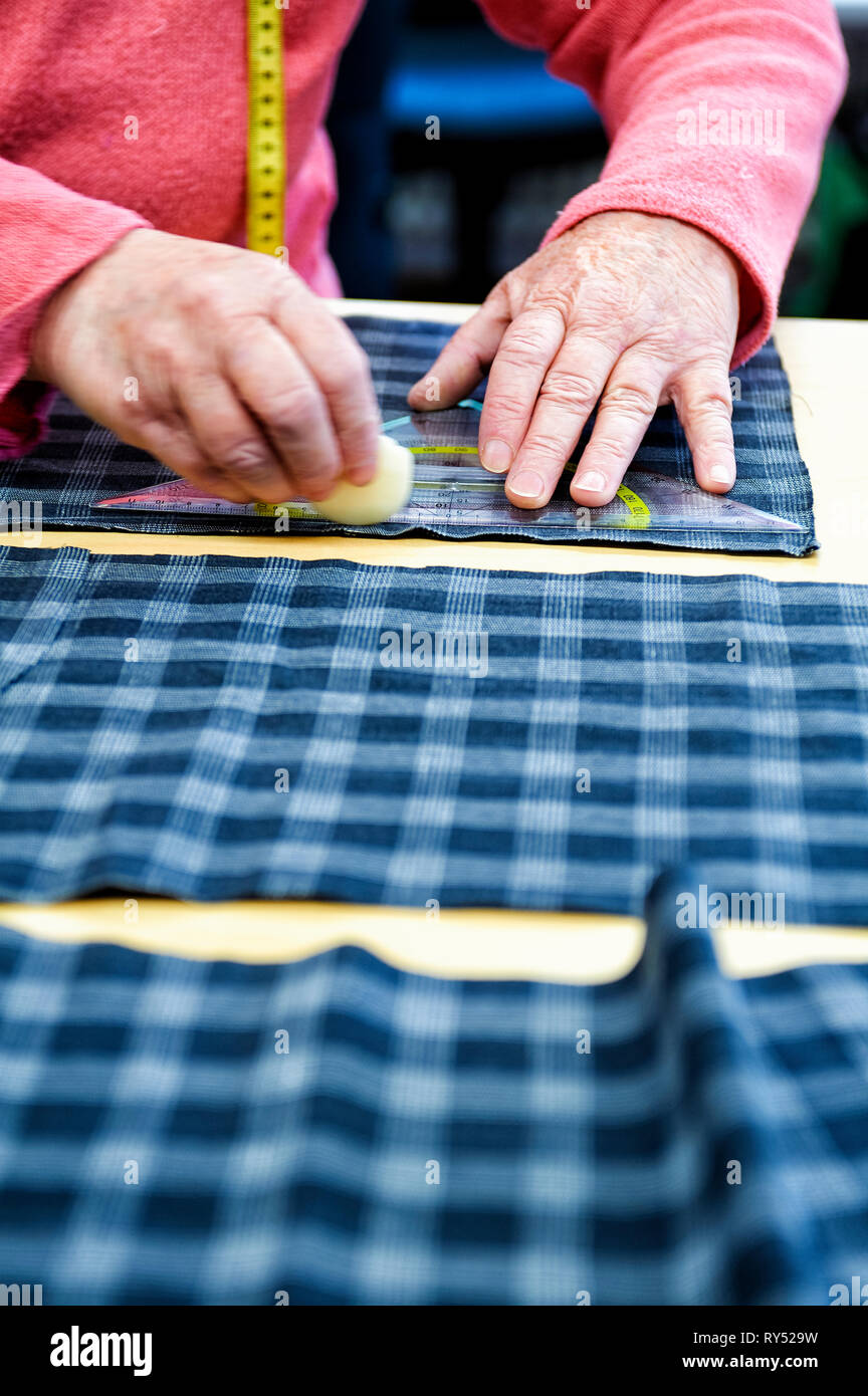 Aeltere Haende einer Schneiderin zeichnen auf Stoff das Schnittmuster an. Stock Photo