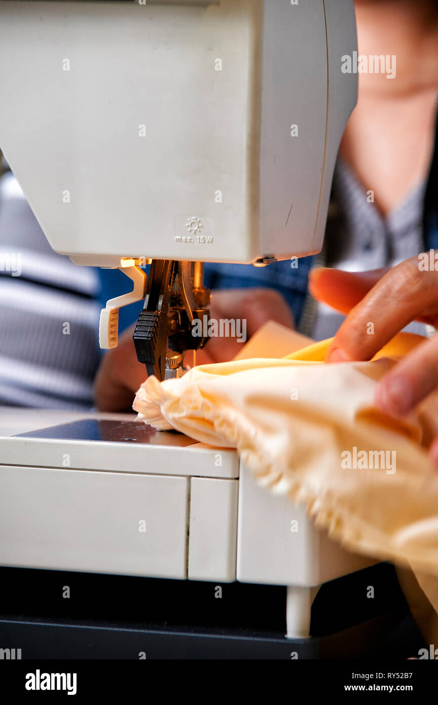 Nahaufnahme einer Schneiderin die an einer Naehmaschine den Stoff unter der Nadel fuehrt beim naehen. Stock Photo