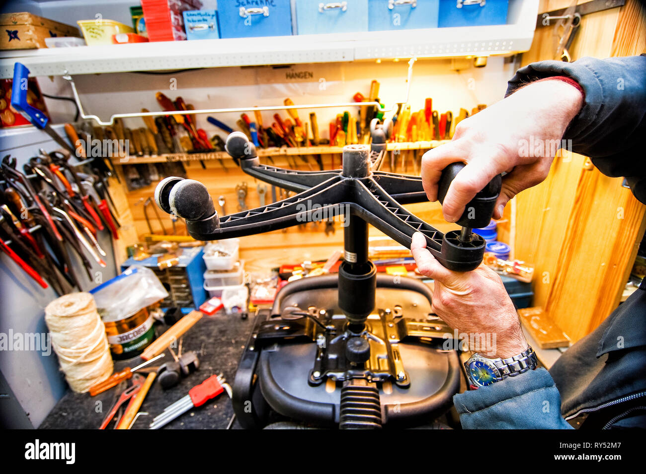 In einer Werkstatt wird das Rad an einem Buerostuhl ausgewechsetl. Im Hintergrund ist allerhand Werkzeug zu sehen. Nahaufnahme. Stock Photo