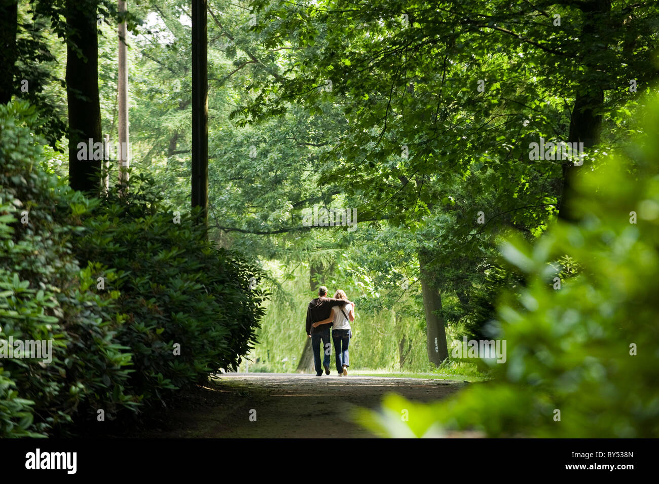 unges Paerchen laeuft Arm in Arm durch einen Park in Gladbeck am Wasserschloss Wittringen. Stock Photo