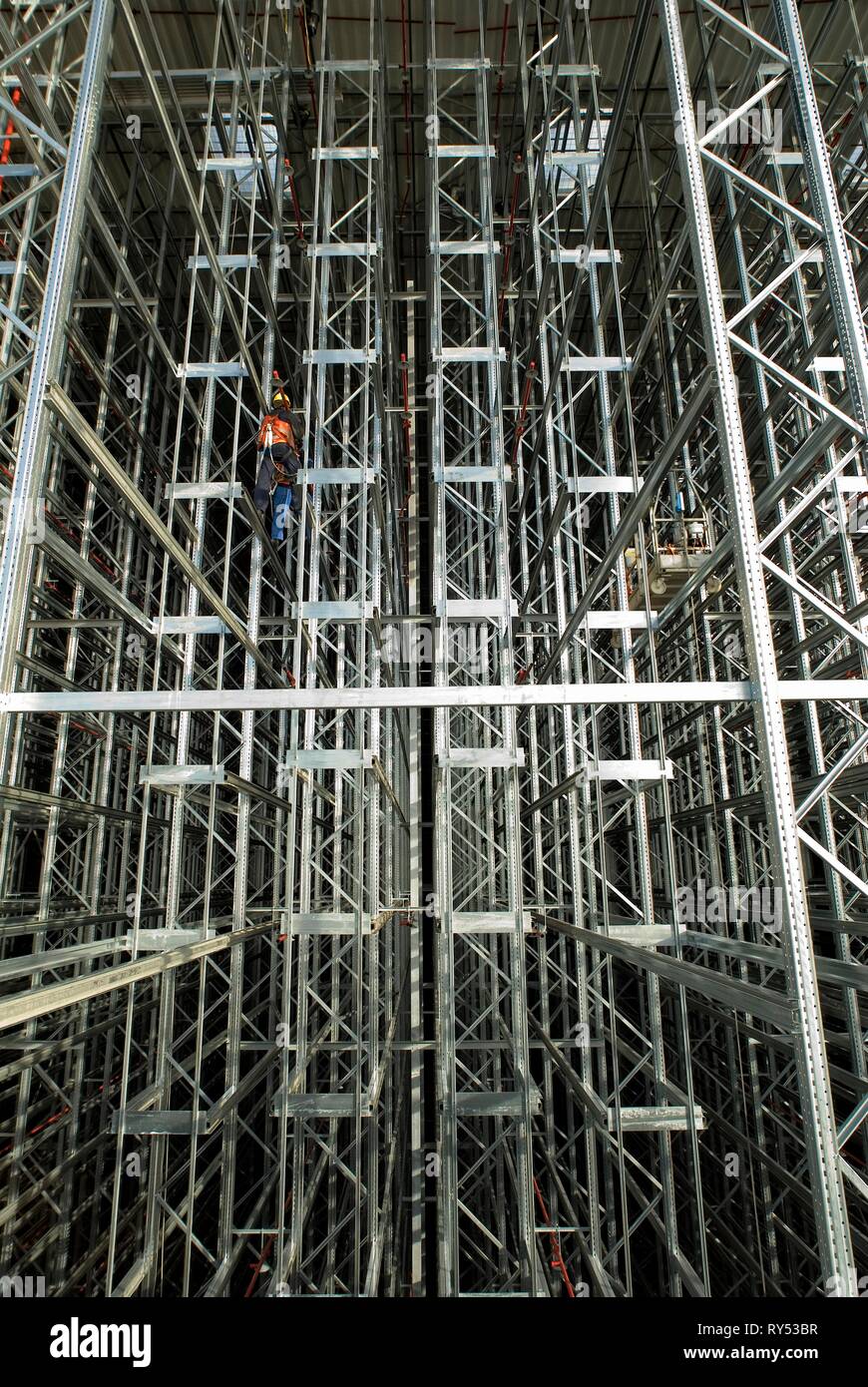 In einer Hochregallandschaft arbeitet ein Bauarbeiter und baut die Hochregale auf. Stock Photo