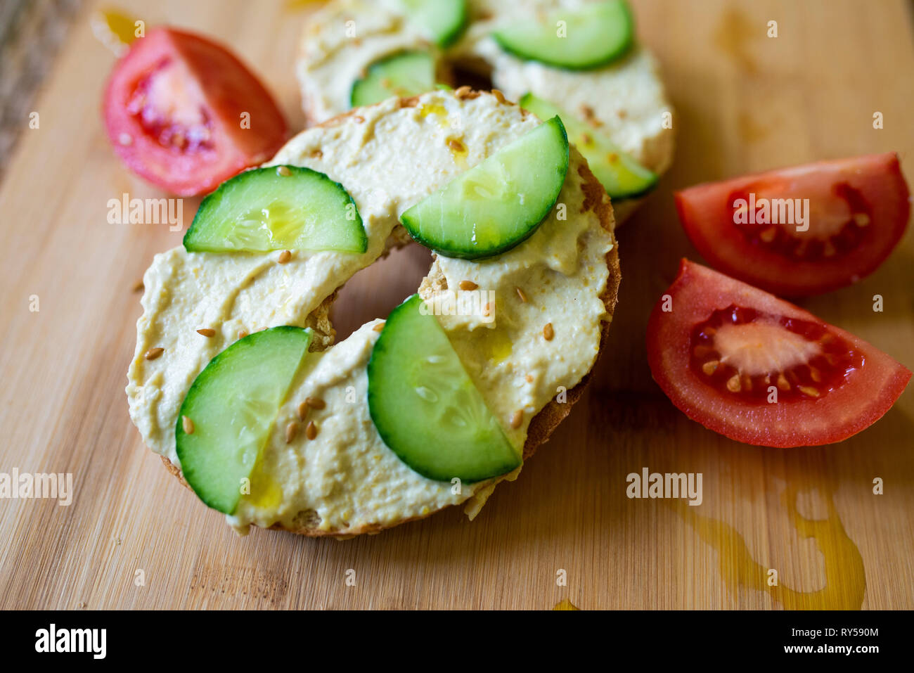 a bagel with hummus, humous, hommous and cucumber, vegan, vegetarian, healthy food breakfast or lunch on a wooden board Stock Photo