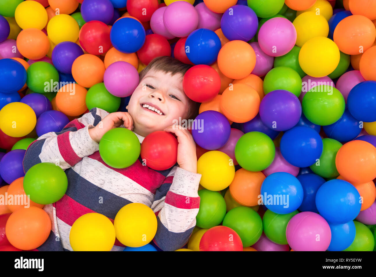 Little boy playing in the pool with plastic balls in the nursery. Indoors activities for