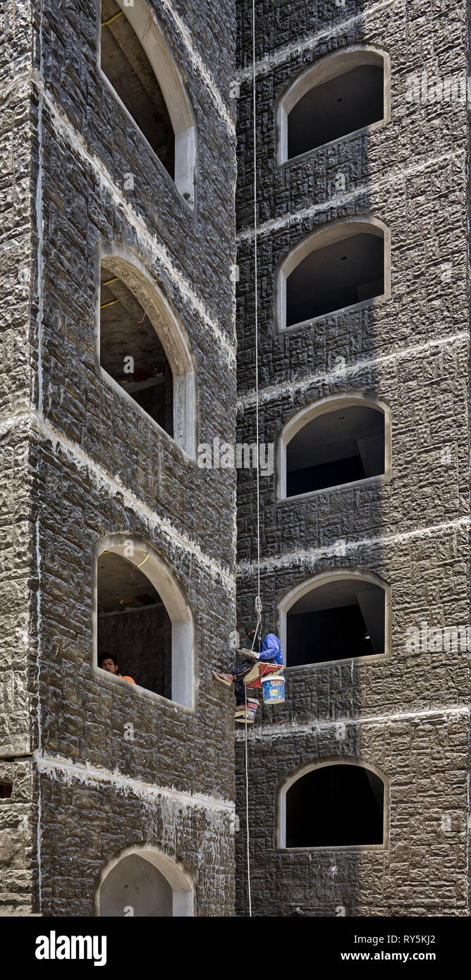 Construction worker suspended on a safety harness whilst pointing an exterior wall. Thailand Southeast Asia Stock Photo
