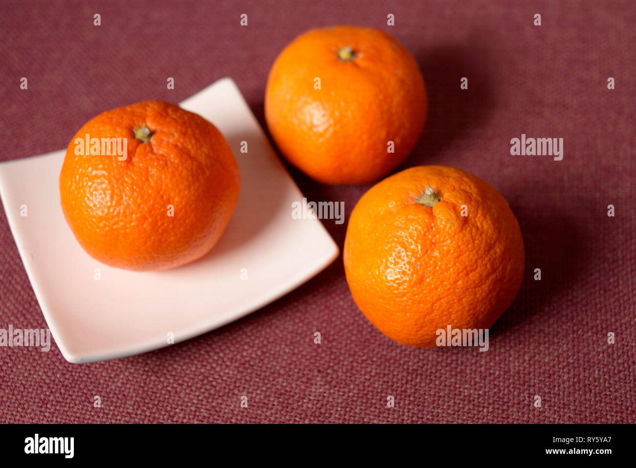 Three oranges n a plate placed on red textile, studio closeup Stock Photo
