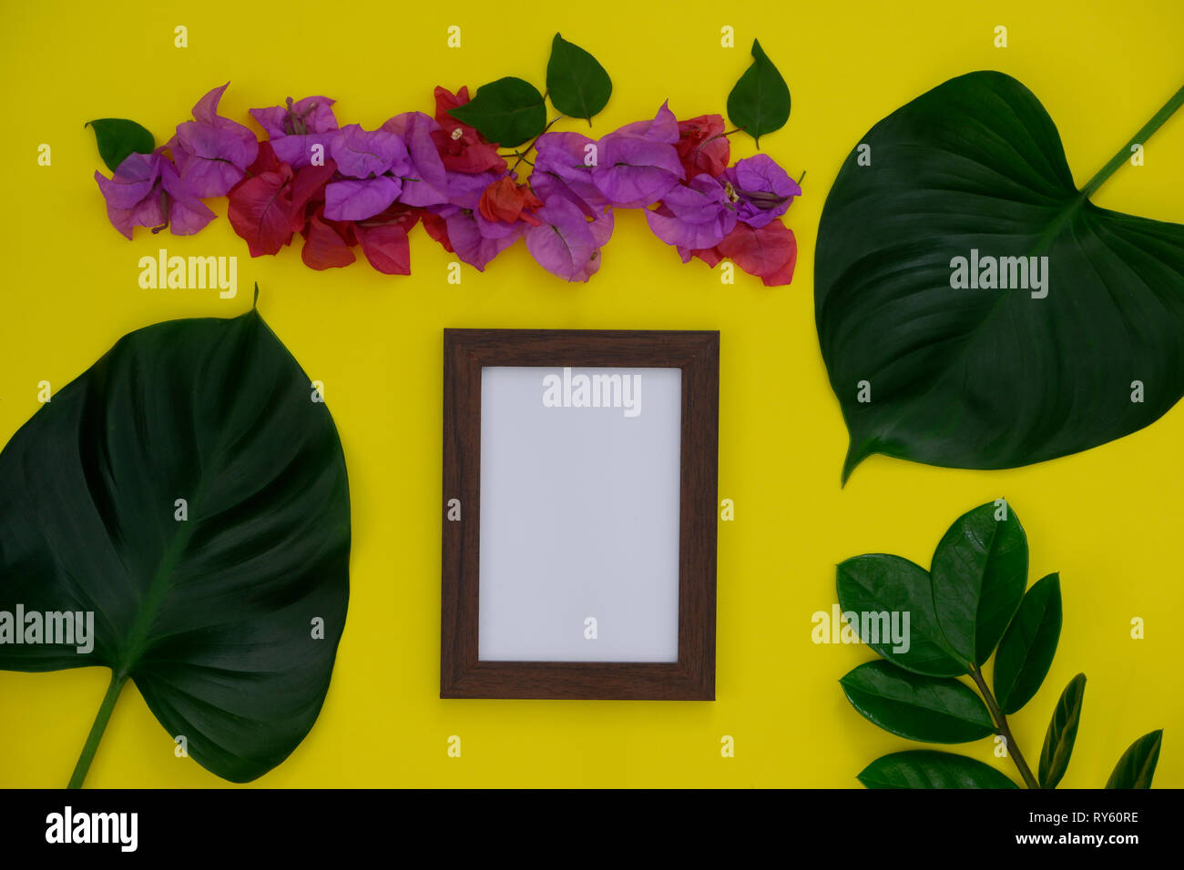 Mock-up photo frame with space for text or picture on yellow background and tropical leaf and flower. Stock Photo
