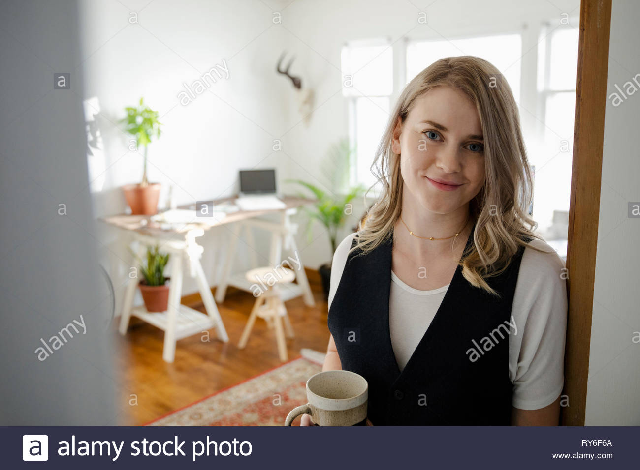 Portrait confident woman drinking coffee in home office doorway Stock Photo