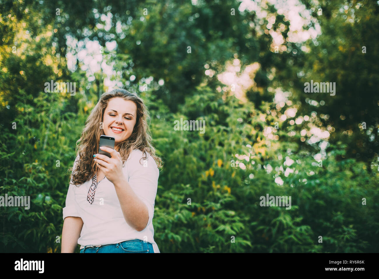 Young Beautiful Pretty Plus Size Caucasian Girl Woman Dressed In White Blouse And Blue Jeans Enjoying Life, Smiling And Using Smartphone Standing On S Stock Photo