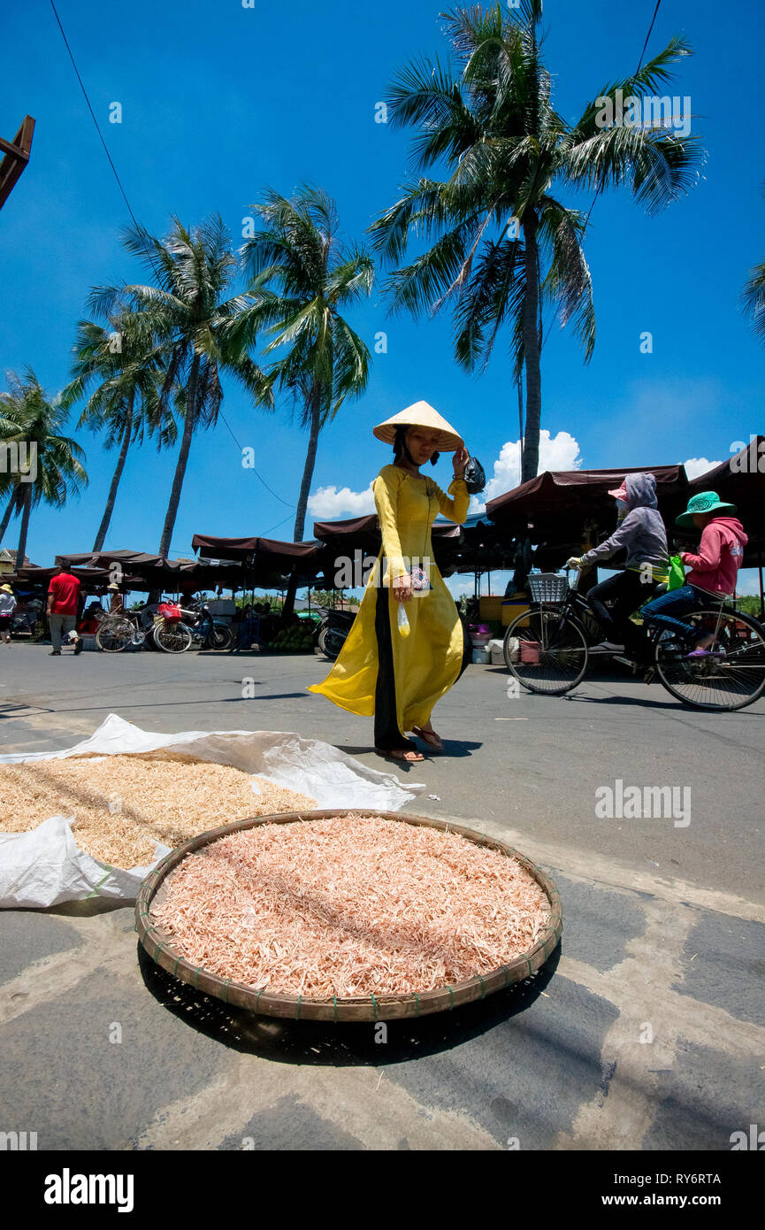 Vietnamese Girl Walking in Yellow Au Dai dress and Conical Hat - Hoi An Market, Vietnam Stock Photo