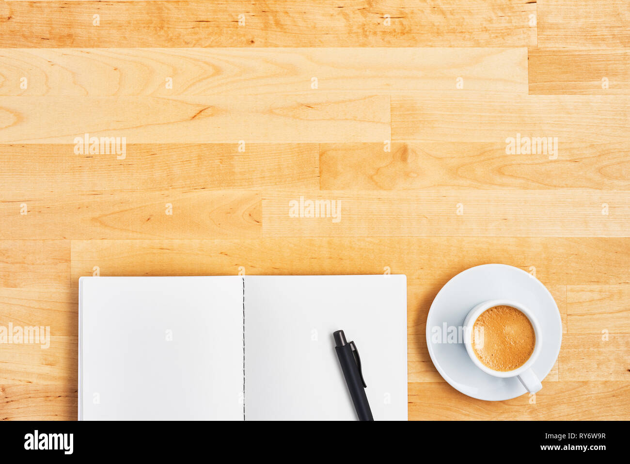 Office desk with blank notebook, pen and cup of coffee or espresso on yellow wooden table. Top view. Copy space for text. Flat lay. Stock Photo