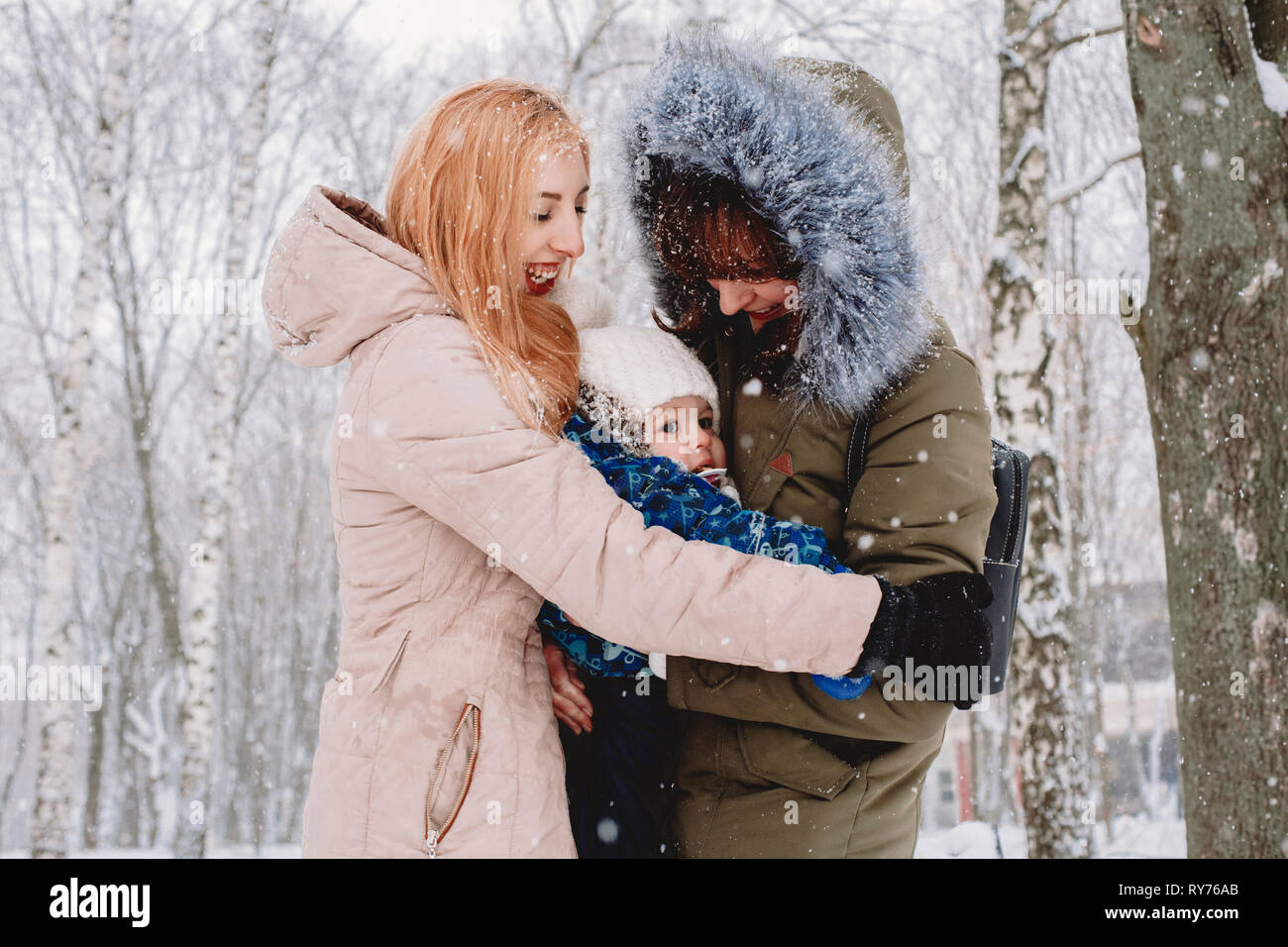 Happy mothers embracing son while standing against trees in park during snowfall Stock Photo
