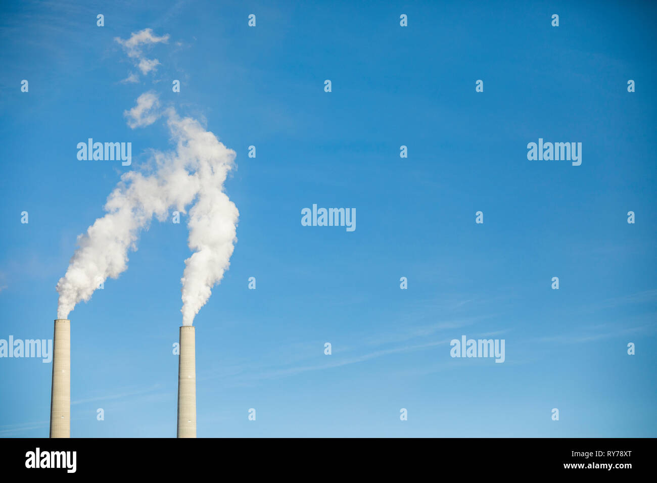 Low angle view of smoke emitting from chimneys against blue sky Stock Photo