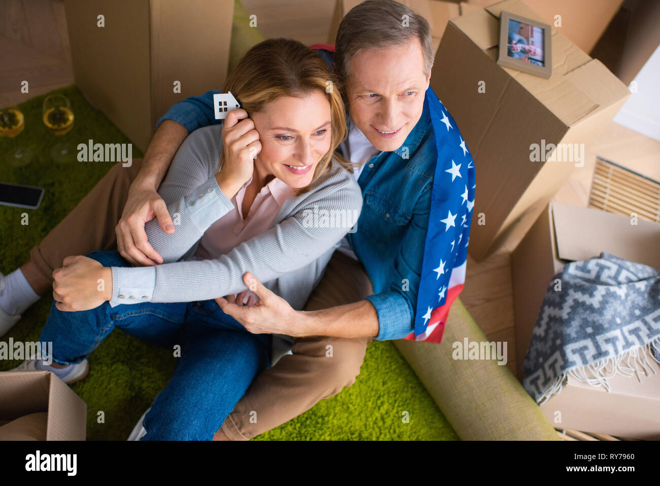 happy woman holding keys with house model trinket while sitting on floor with husband Stock Photo