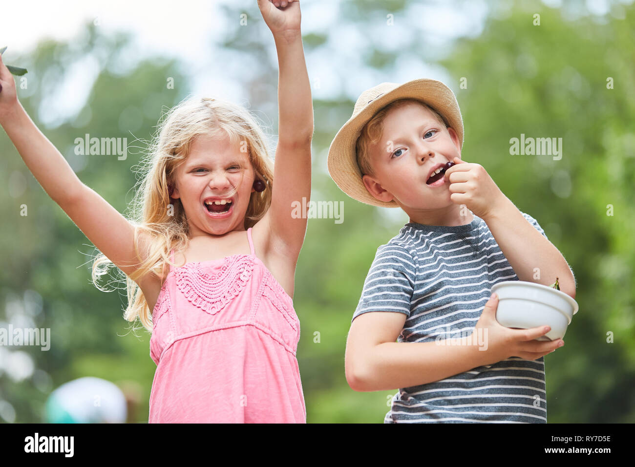 Two kids at a summer party on vacation are having fun and eating cherries Stock Photo