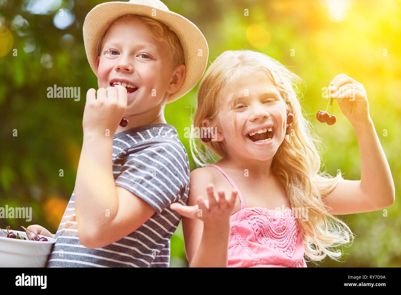 Two laughing siblings eat cherries in the summer garden Stock Photo