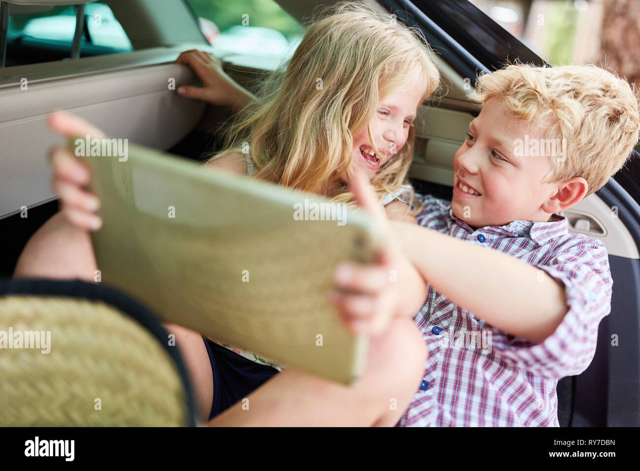 Sibling couple is having fun in the car while playing with the tablet computer Stock Photo